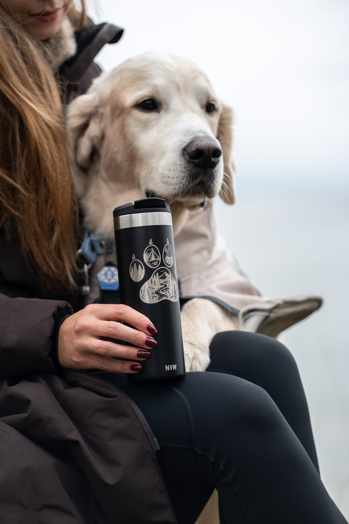 Black Trailmark tumbler held next to a golden retriever